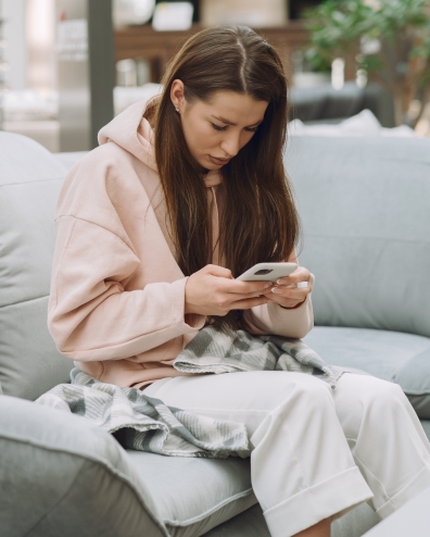 Zieke vrouw zit met een smartphone in haar hand op een bank
