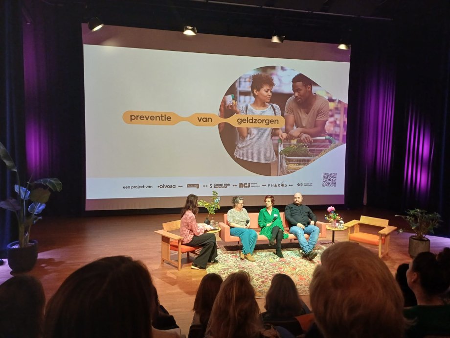 Publiek kijkt naar sprekers op het podium tijdens de kick-off van het programma Preventie van geldzorgen